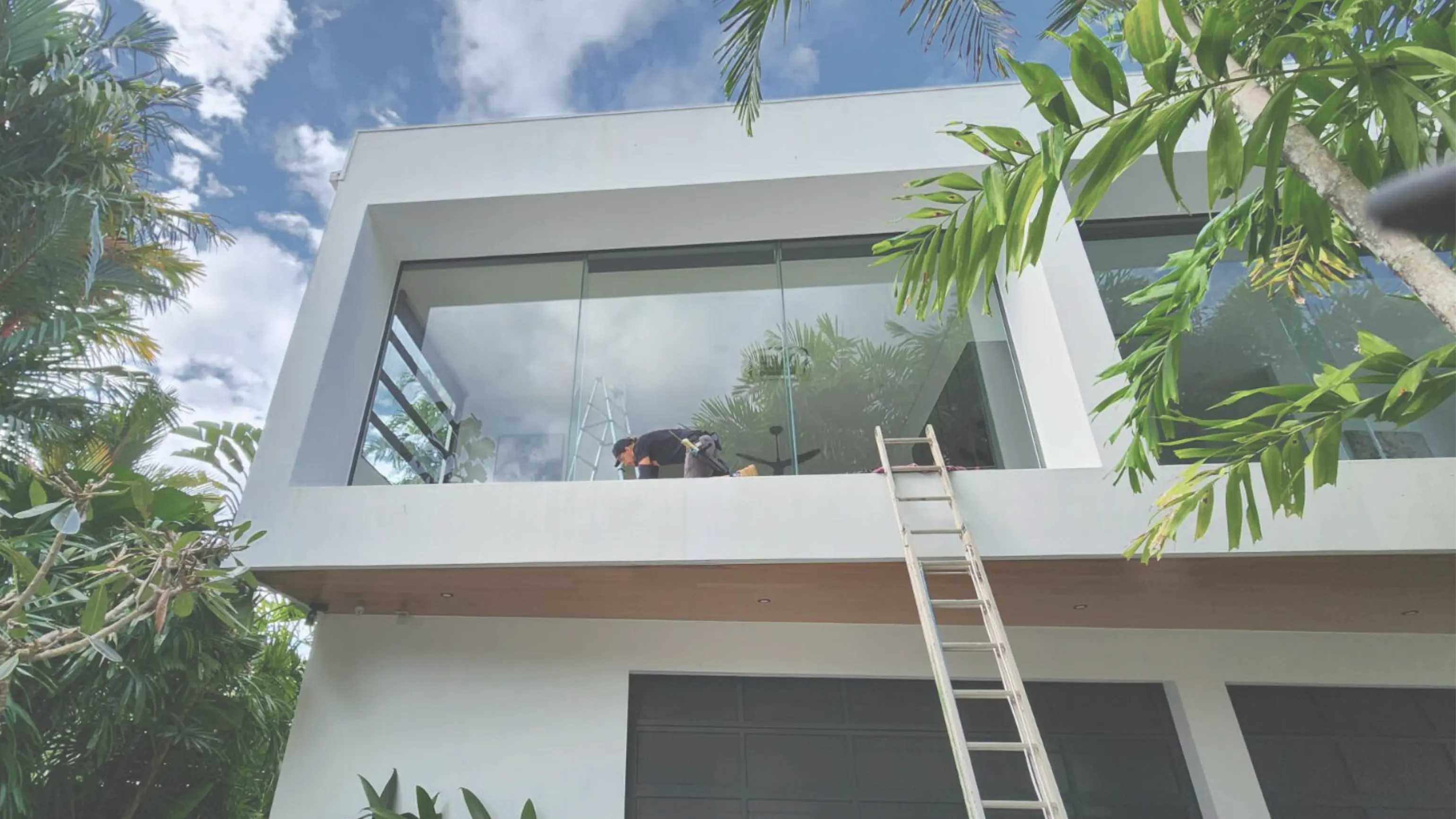Wish You Were Clear technician cleaning upper-storey glass from a balcony on a two-storey Cairns home