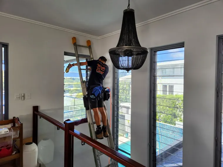 Wish You Were Clear technician on a ladder cleaning tall interior windows beside a chandelier